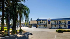 Un motel avec un parking, un bâtiment doté d’un toit bleu et des palmiers.