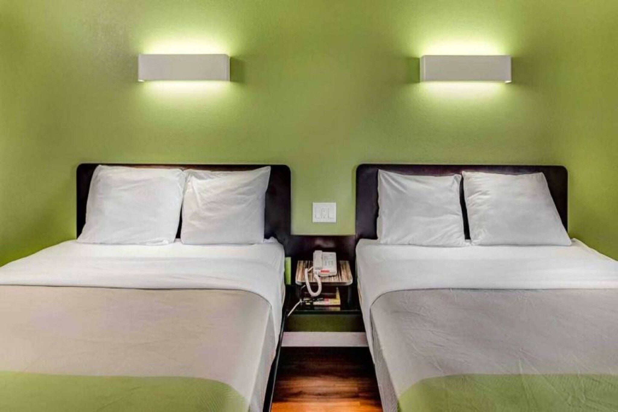 Une chambre avec deux lits, une table de chevet avec un téléphone et des murs verts.