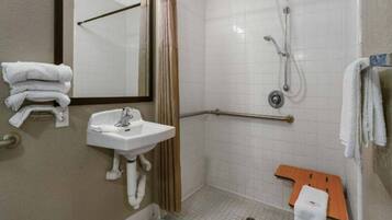 A bathroom with a white sink, a shower with a grab bar, and a wooden bench.