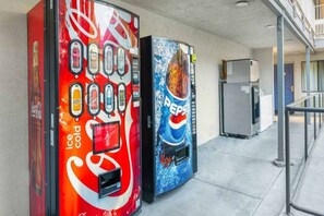 Vending machines with various beverage options, including Coca-Cola and Pepsi, in a commercial area.
