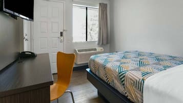 Une chambre à coucher comprenant un lit, un bureau, une chaise, un téléviseur, une fenêtre avec des rideaux et un appareil de climatisation.