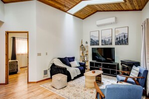 A modern living room with a wooden ceiling, a sofa, a TV, and a bookshelf. - Hike, Paddle & Relax: Cabin By Cle Elum Lake (Ronald)