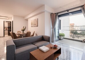 A modern living room with a grey sofa, a wooden coffee table, and a dining area with chairs and a table. - Spacious 3BR Family Stay in Dist 1 _ Pool, Gym & Balcony (Thành phố Hồ Chí Minh)