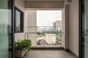 A narrow balcony with a glass door, a potted plant, and a view of a cityscape with high-rise buildings. - Spacious 3BR Family Stay in Dist 1 _ Pool, Gym & Balcony (Thành phố Hồ Chí Minh)