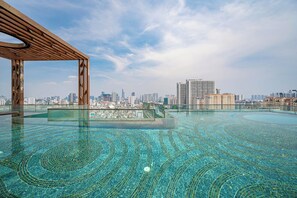 An infinity pool with a cityscape view, a wooden pergola, and a clear sky. - Spacious 3BR Family Stay in Dist 1 _ Pool, Gym & Balcony (Thành phố Hồ Chí Minh)