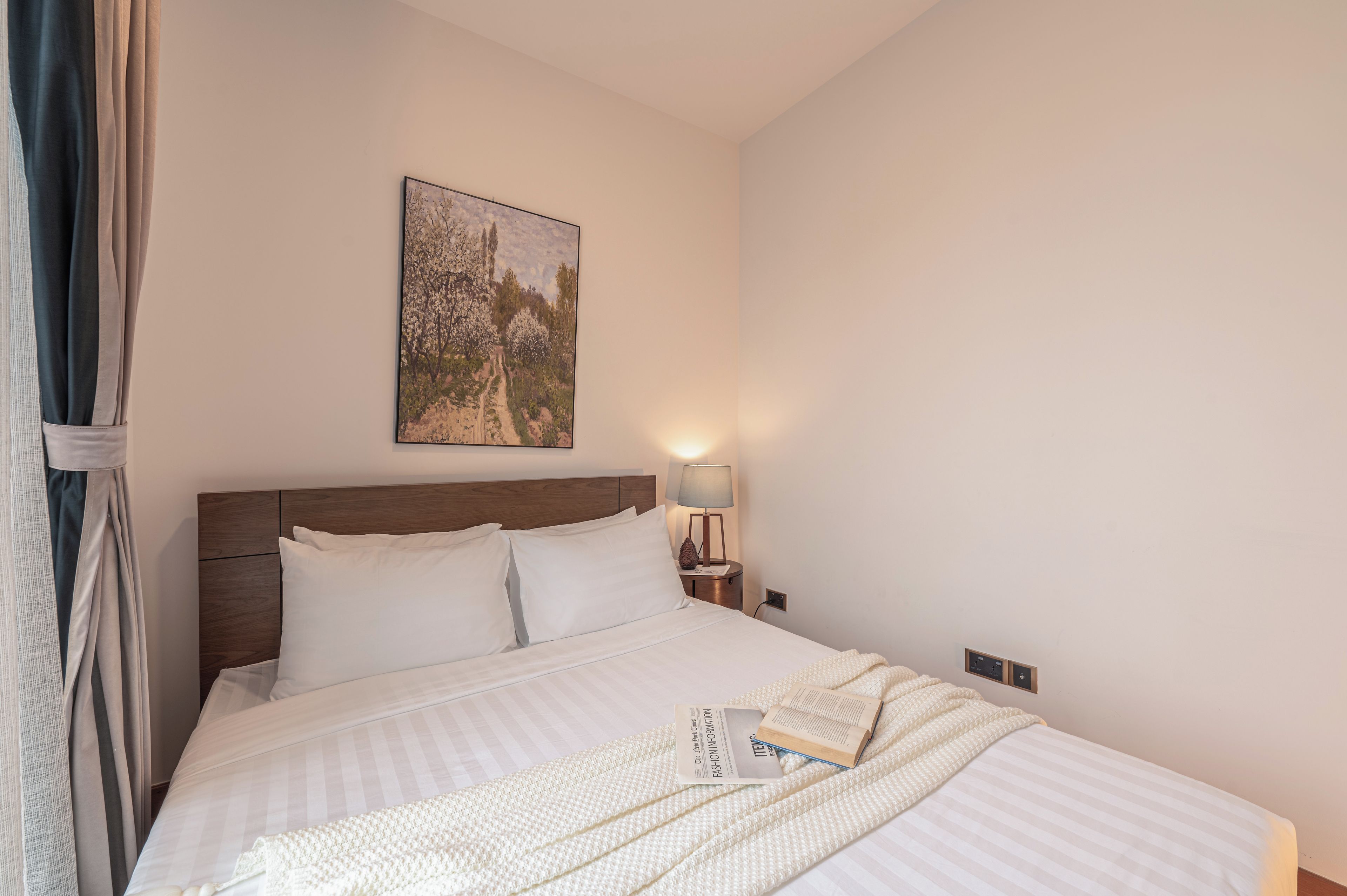 A neatly made bed with a pillow, a bedside lamp, and a framed picture on the wall.