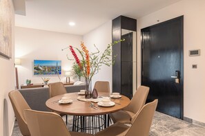 A dining area with a round table, six chairs, a vase with flowers, a painting on the wall, and a black door. - Spacious 3BR Family Stay in Dist 1 _ Pool, Gym & Balcony (Thành phố Hồ Chí Minh)