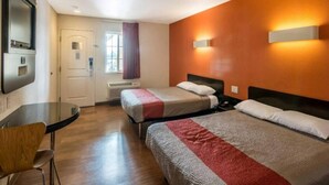 Ein Hotelzimmer mit zwei Betten, einem Schreibtisch und einem Stuhl. Es gibt ein Fenster mit Vorhängen, eine Tür und eine Wandleuchte.