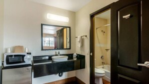 Ein Badezimmer mit Waschbecken, Spiegel, Toilette, Dusche und einer Mikrowelle auf einer Ablagefläche.