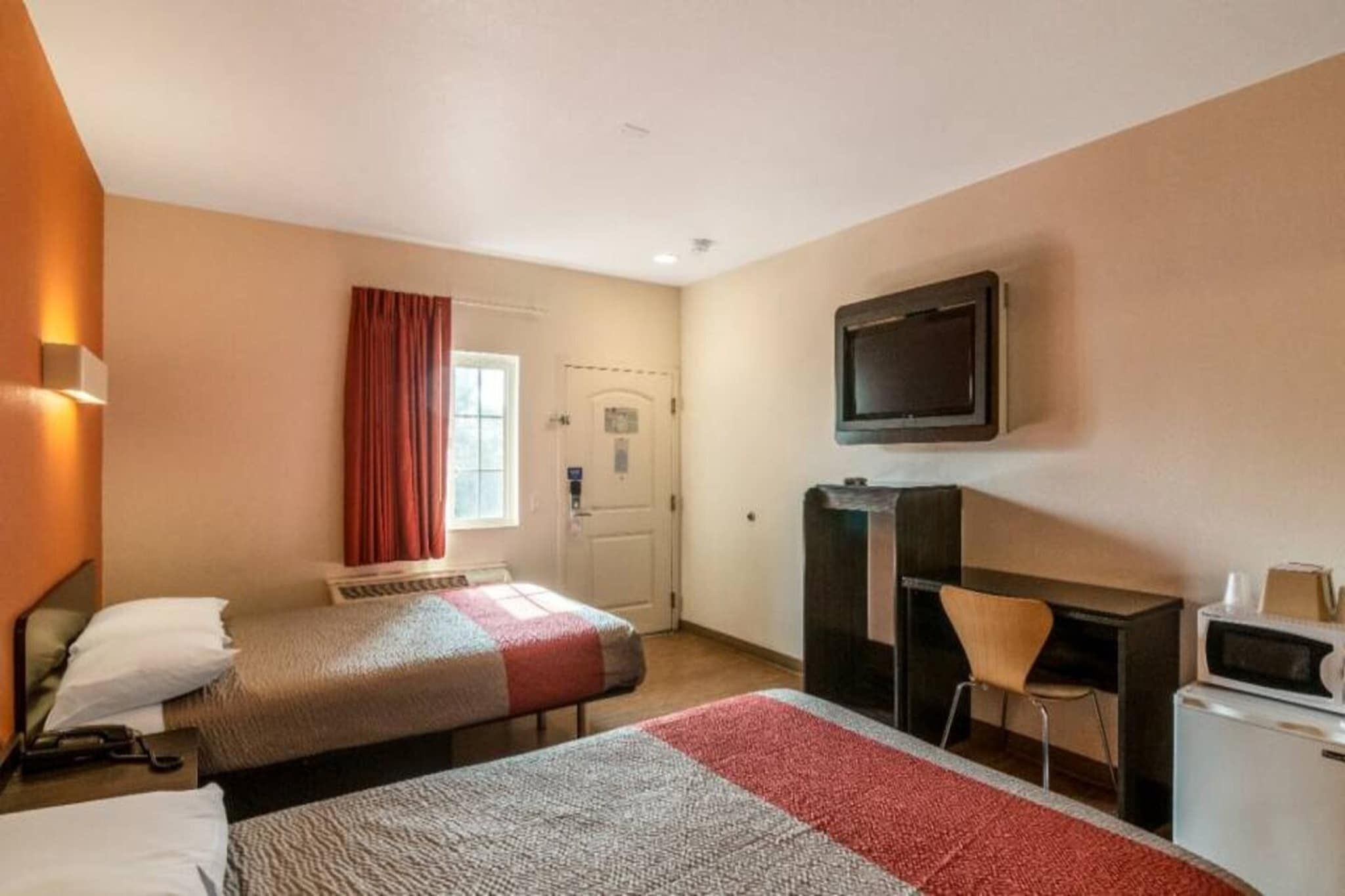 A hotel room with two beds, a desk, a chair, a television, and a microwave.