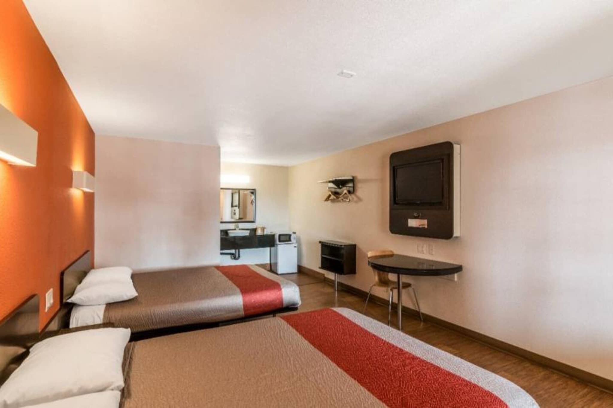 Quarto de hotel com duas camas, uma cozinha compacta, televisão e escrivaninha.