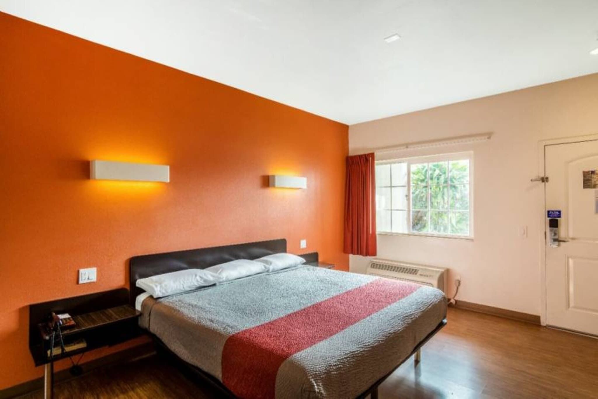 Ein Hotelzimmer mit Bett, Nachttisch, einem Fenster mit Vorhängen und einer Tür.