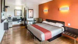 A hotel room with a bed, a desk, a chair, a mirror, and a bathroom. - 1 King Bed | Non-Smoking, Micfridge (Bell Gardens)