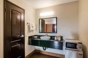 Un baño con una puerta de madera oscura, un lavabo blanco, un espejo sobre el lavabo y un microondas a la derecha.