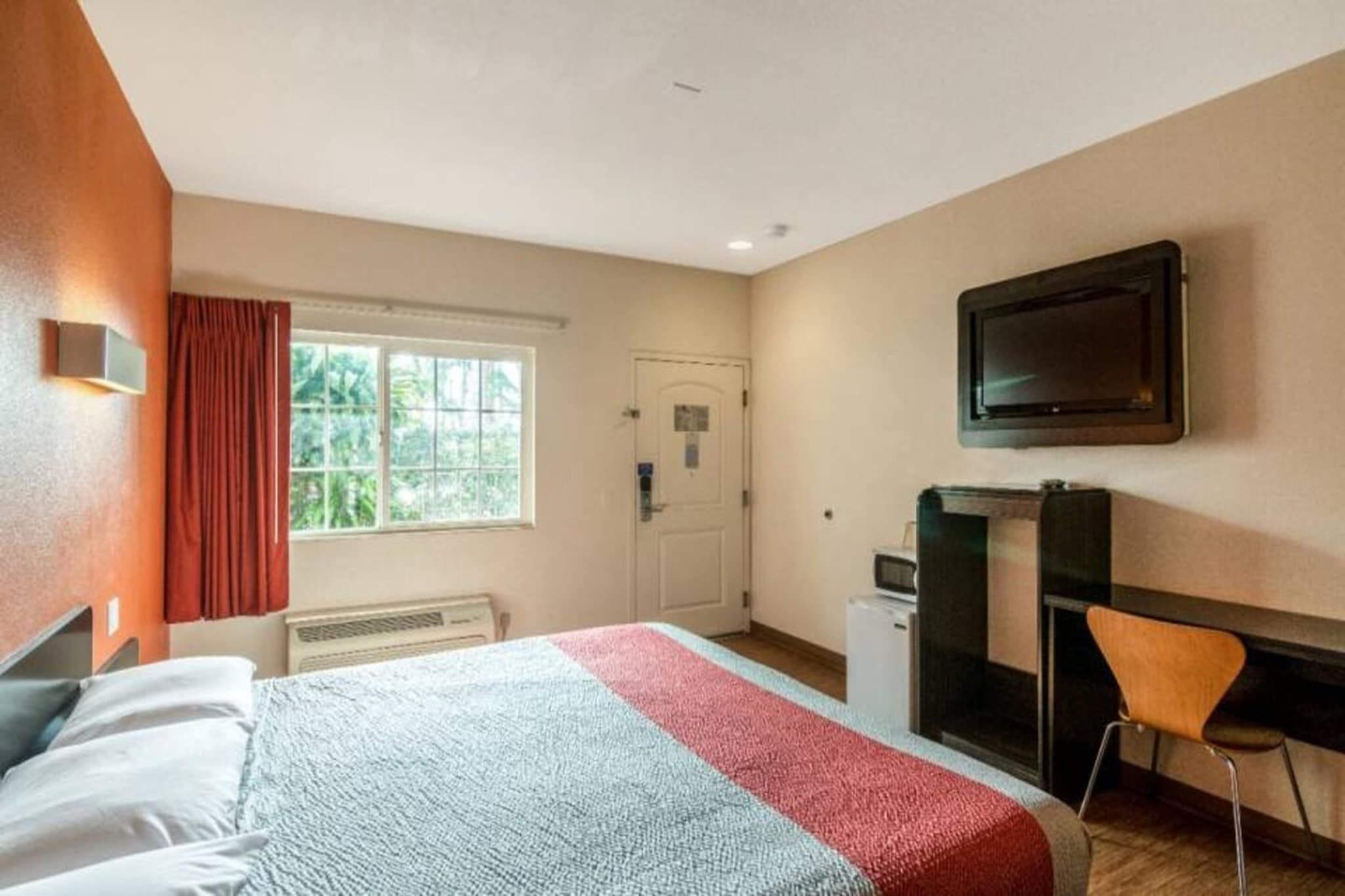 Ein Hotelzimmer mit einem Bett, einem Schreibtisch, einem Sessel, einem Fernseher und einem Fenster mit Vorhängen.