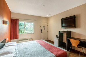 A hotel room with a bed, a desk, a chair, a television, and a window with curtains. - 1 King Bed | Smoking, Micfridge (Bell Gardens)