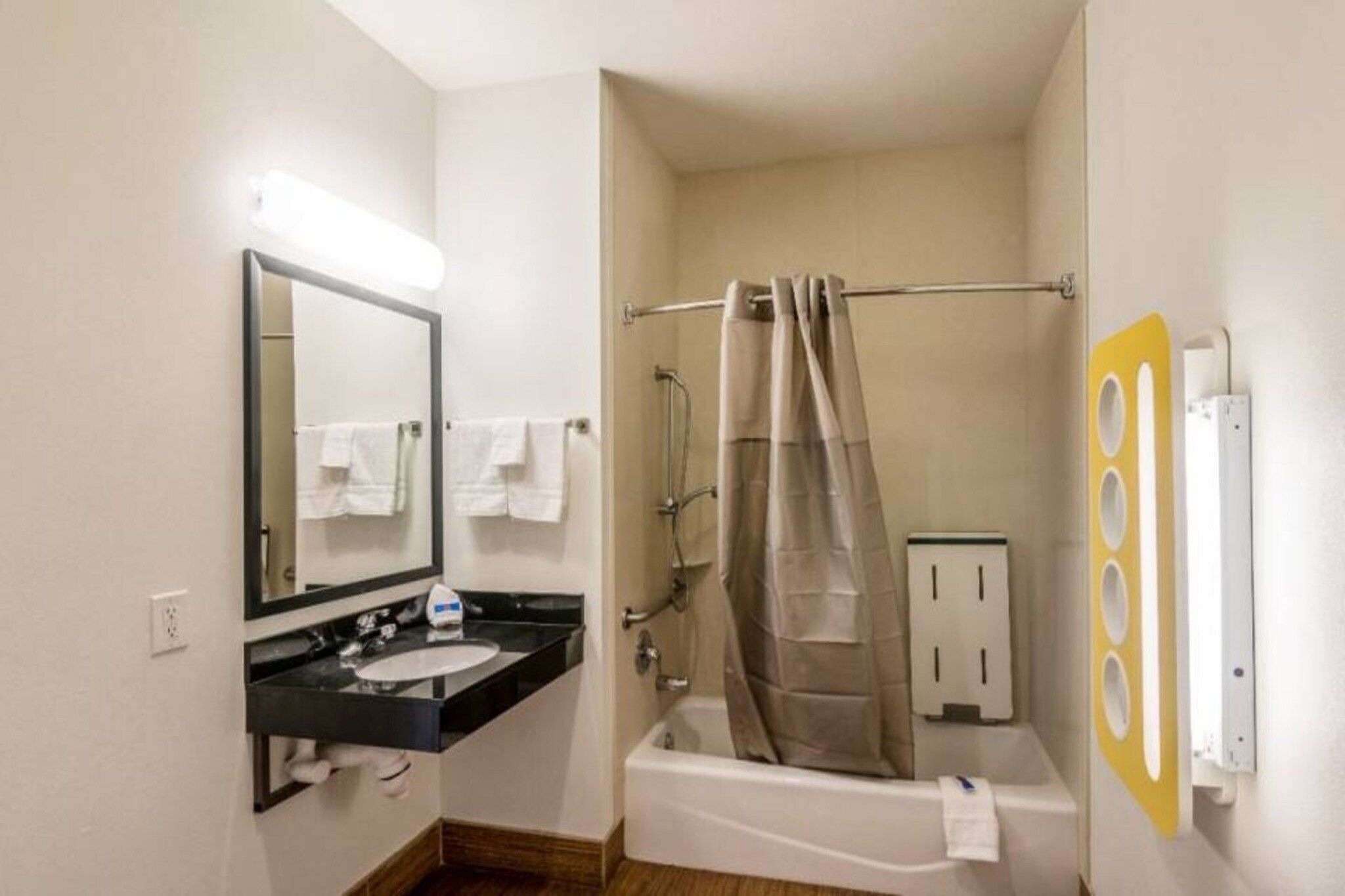 A compact hotel bathroom with a sink, mirror, shower, and towel rack.