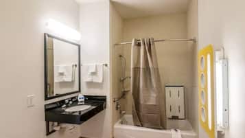 A compact hotel bathroom with a sink, mirror, shower, and towel rack.