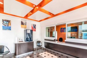 Un área de recepción con mostrador, máquina de café, refrigerador y una silla.