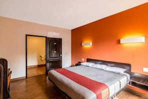 Una habitación de hotel con una cama, un escritorio, una silla y una puerta que da a otra habitación.