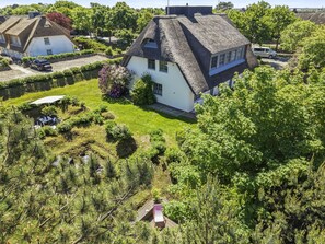 Ein Haus mit einem Reetdach, umgeben von einem gepflegten Garten mit verschiedenen Pflanzen und einem kleinen Teich.