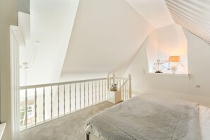 Ein Schlafzimmer mit schrägen Wänden, einem Fenster mit Lampe und Blick ins Freie.