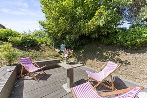Eine Terrasse mit zwei gestreiften Liegestühlen und einem Tisch mit Blumenvase und einem Weinglas.