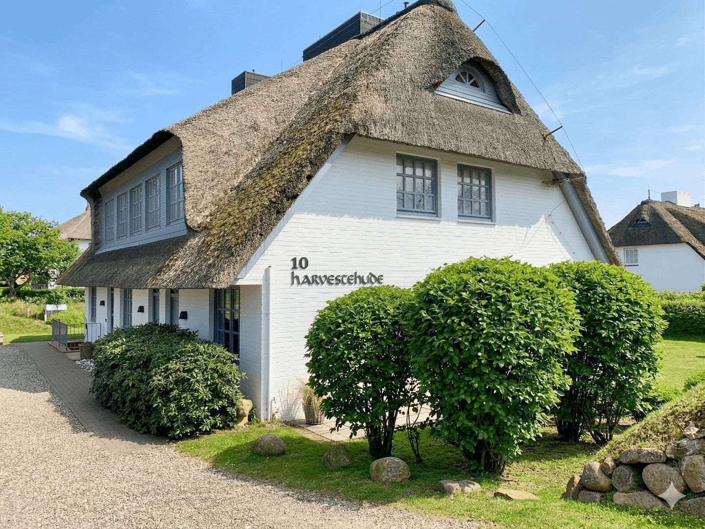 Une maison traditionnelle à toit de chaume, avec une pancarte indiquant « 10 Harvesthuide » et une allée gravillonnée.