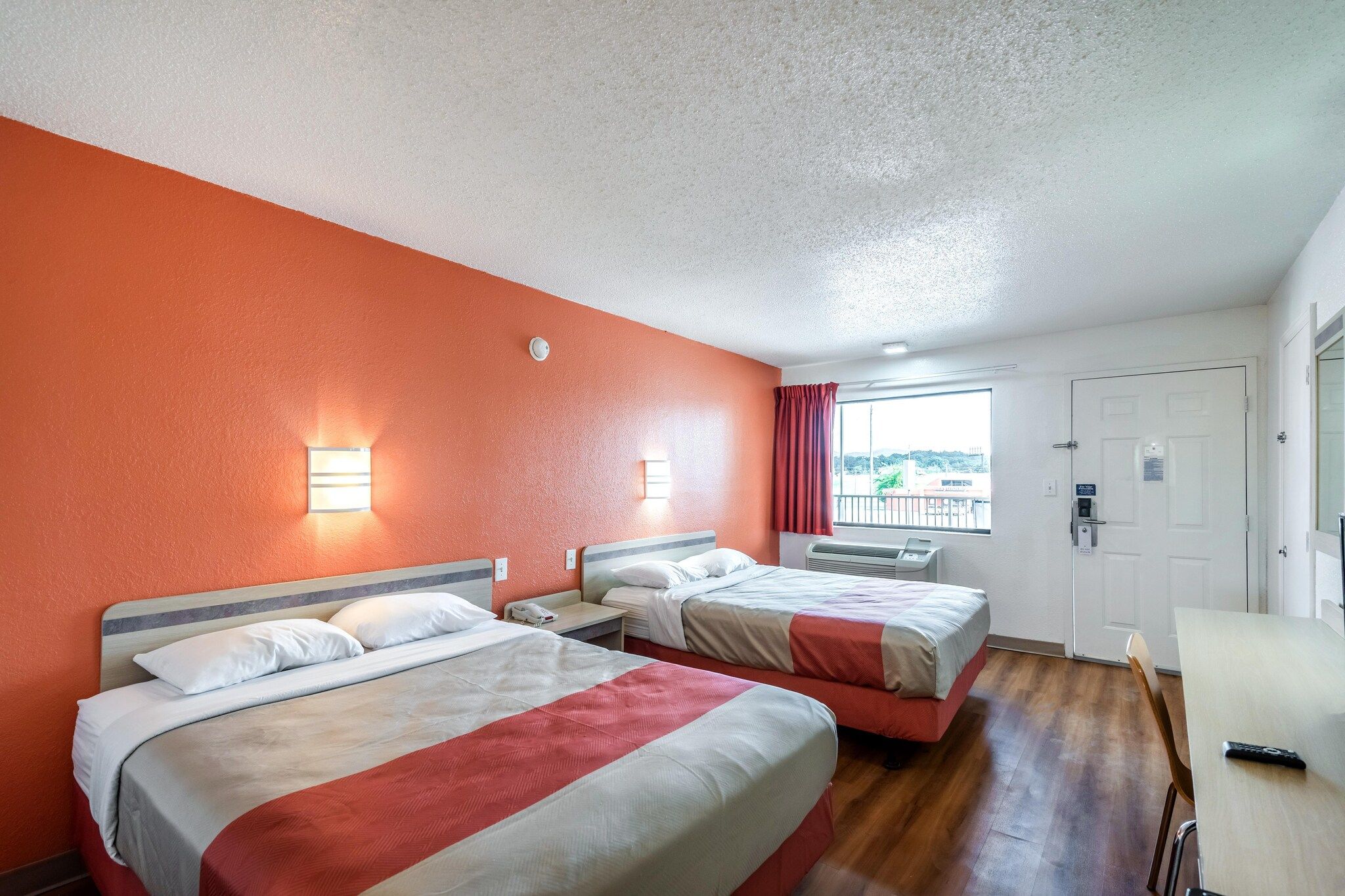 Een hotelkamer met twee bedden, een bureau, een stoel, een raam met gordijnen en een deur.