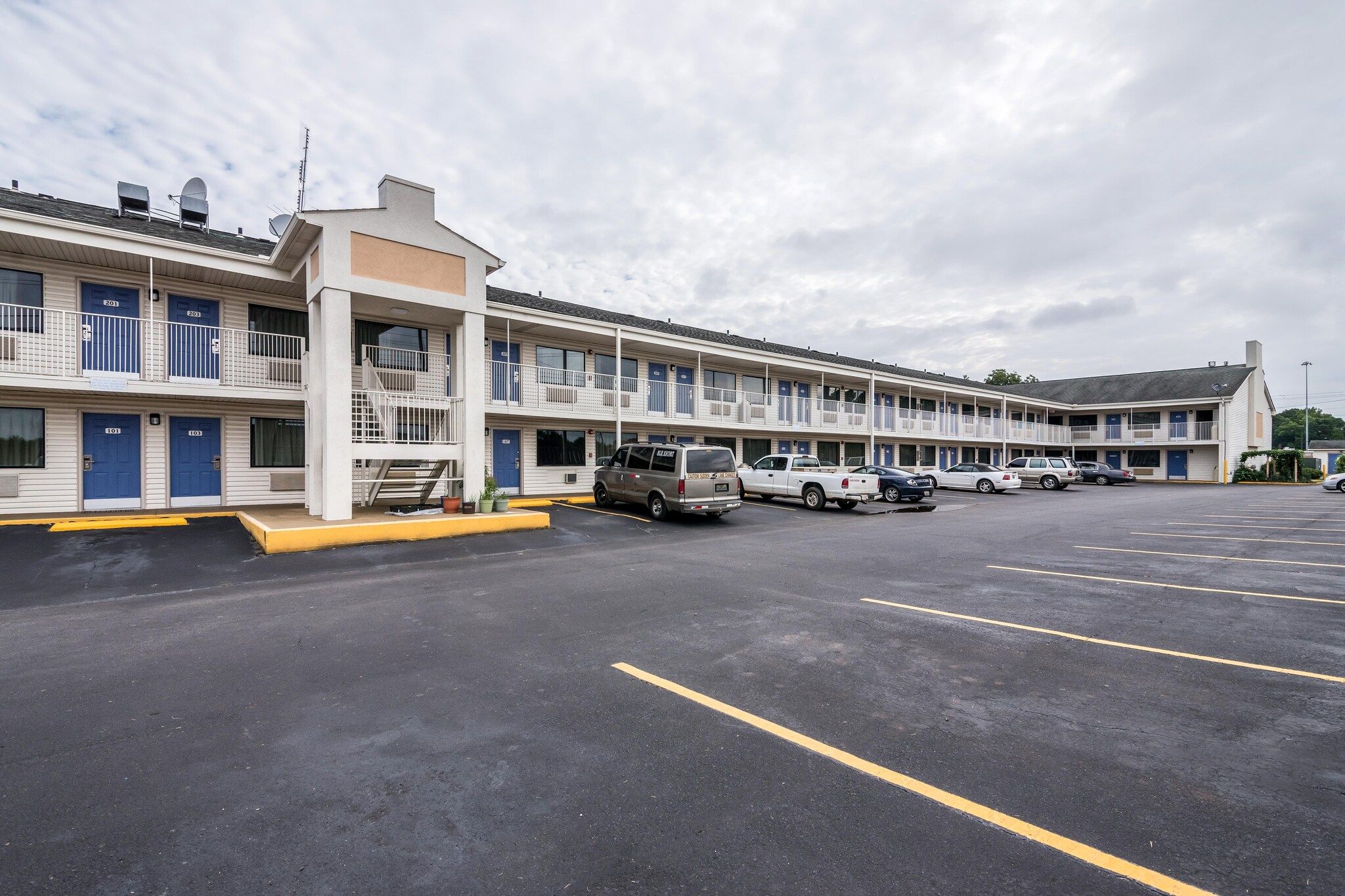 Ein Motel mit mehreren Zimmern, einem Parkplatz und einigen parkenden Fahrzeugen.