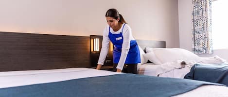 Ein Hotelzimmer mit einem ordentlich bezogenen Bett, einem Nachttisch mit Lampe und einem gemusterten Vorhang.