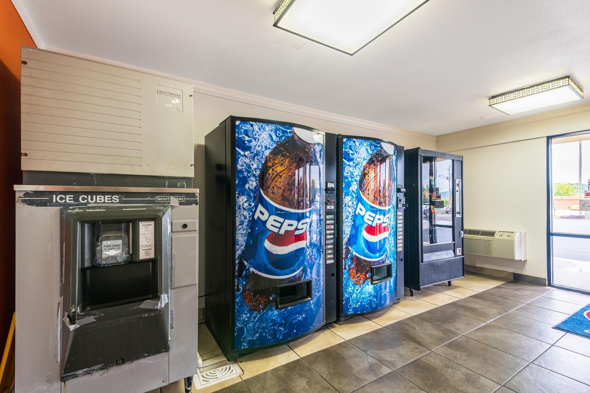 Máquinas expendedoras de Pepsi y cubitos de hielo en una habitación con piso de baldosas y una ventana.