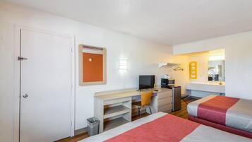 Habitació d'hotel amb llit, escriptori, cadira, televisió i una cuineta petita.