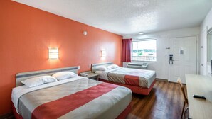 Habitación de hotel con dos camas, un escritorio, una silla, una ventana con cortinas y una puerta.