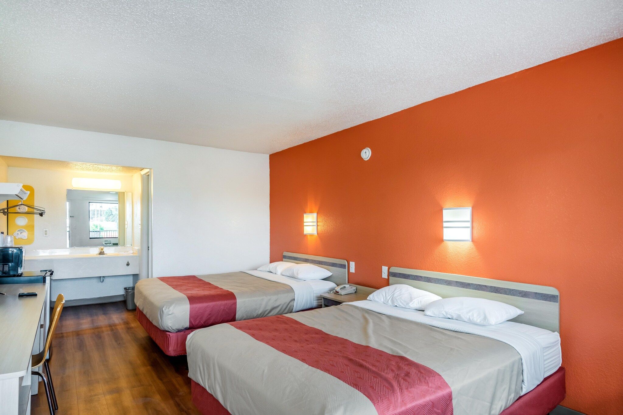 A hotel room with two beds, a desk, a chair, and a bathroom with a mirror.