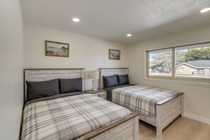 A bedroom with two beds, a window, and two wall-mounted paintings.