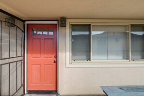 A red door with a mesh screen, a window with blinds, and a concrete step leading to the door.