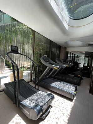 Ein modernes Fitnessstudio mit Laufbändern und einer Glaswand mit Blick auf einen Garten.