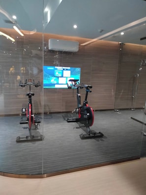Une salle de sport moderne équipée de vélos d’appartement, d’un grand écran affichant des informations sur les exercices et d’une paroi en verre.
