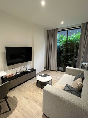 Ein modernes Wohnzimmer mit einem Flachbildfernseher, einer Couch, einem Couchtisch und einem Fenster mit Vorhängen.