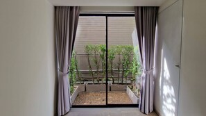 Blick durch eine Schiebetür auf einen Balkon mit Pflanzen und eine Kiesfläche.