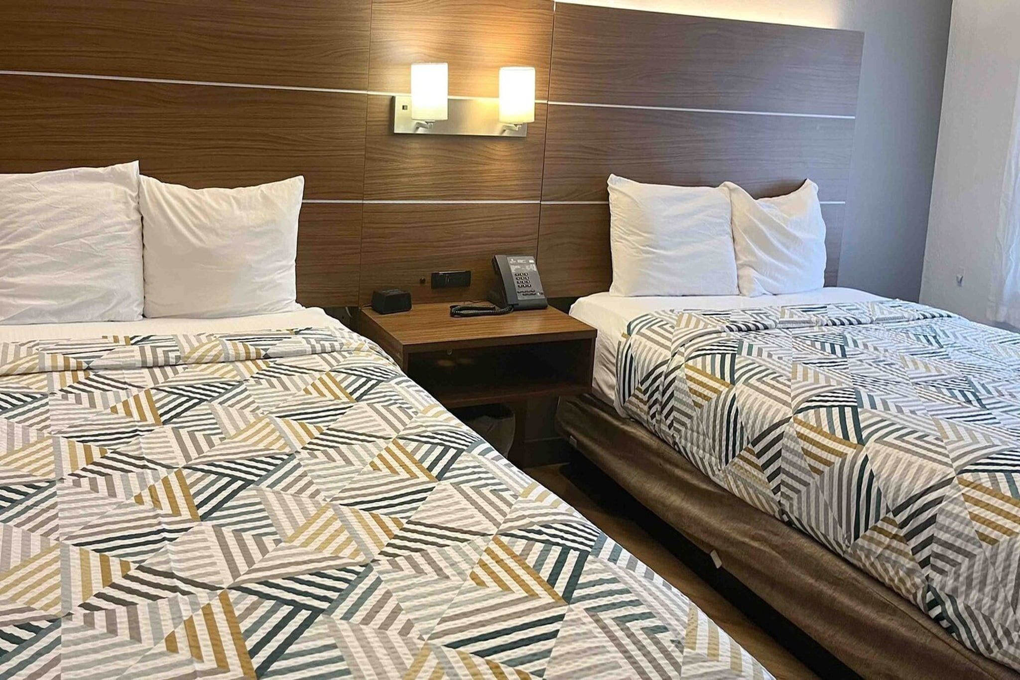 Een hotelkamer met twee bedden, elk met een beddekleed met een patroon, een houten hoofdbord en een nachtkastje met telefoon en lamp.