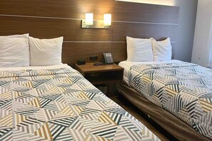 Ein Hotelzimmer mit zwei Betten, jeweils mit einem gemusterten Überwurf, einem Holzkopfstück und einem Nachttisch mit Telefon und Lampe.