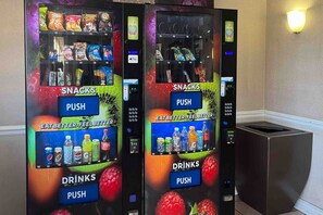 Zwei Verkaufsautomaten mit Snacks und Getränken, beschriftet mit 'SNACKS' bzw. 'DRINKS', jeweils mit einem 'PUSH'-Knopf.