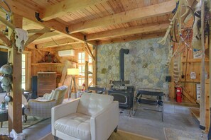 A cozy cabin interior with a stone wall, wooden beams, a fireplace, and a comfortable seating area. - Fire Pit, Deck! Rural Retreat Near East Beach (Charlestown)