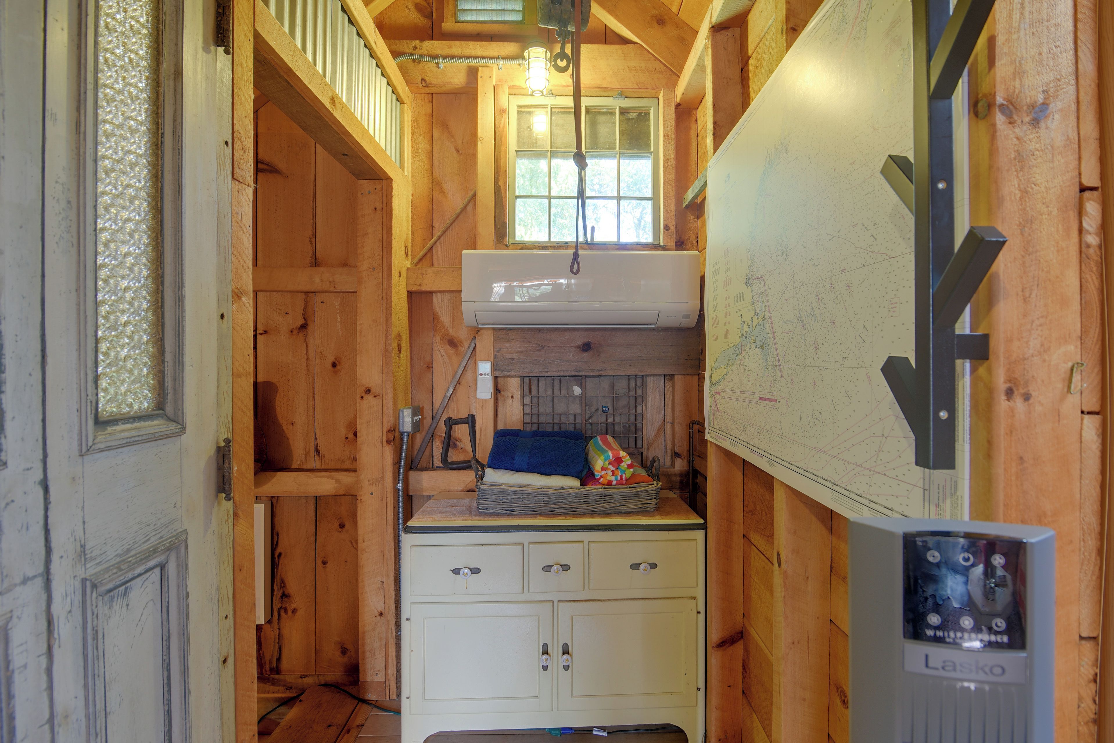 Una habitación pequeña de madera con un equipo de aire acondicionado blanco, una ventana y un mapa en la pared.