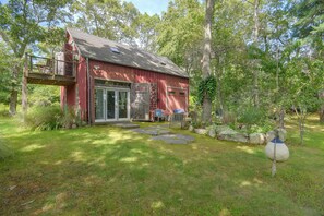 A red wooden cabin with a deck, a glass door entrance, and a stone pathway leading to a seating area with a table and chairs. - Fire Pit, Deck! Rural Retreat Near East Beach (Charlestown)