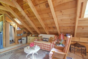 A cozy attic room with a high wooden ceiling, a sofa, a chair, a small table, and a lamp. - Fire Pit, Deck! Rural Retreat Near East Beach (Charlestown)