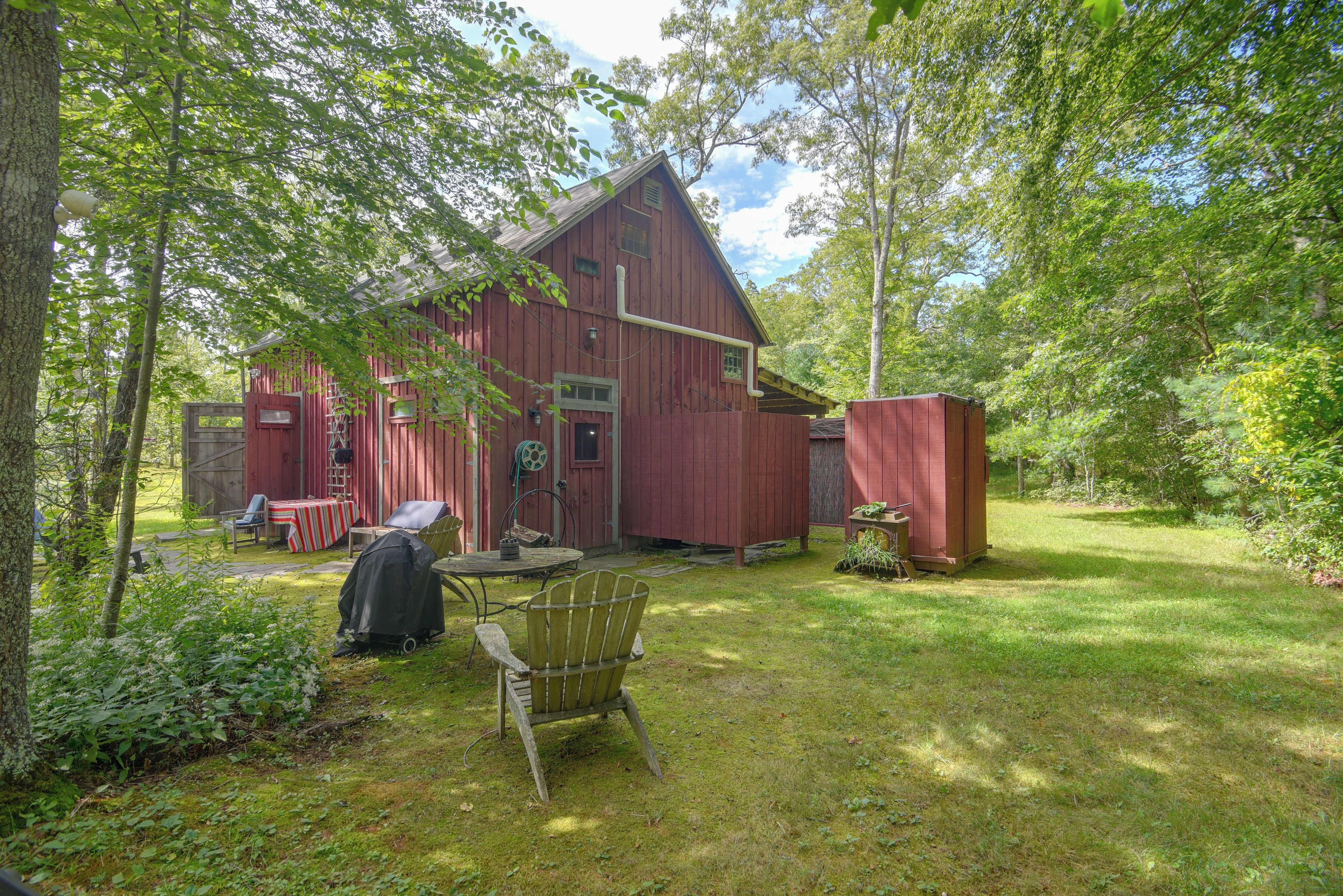 A red wooden house with a porch, surrounded by lush greenery.