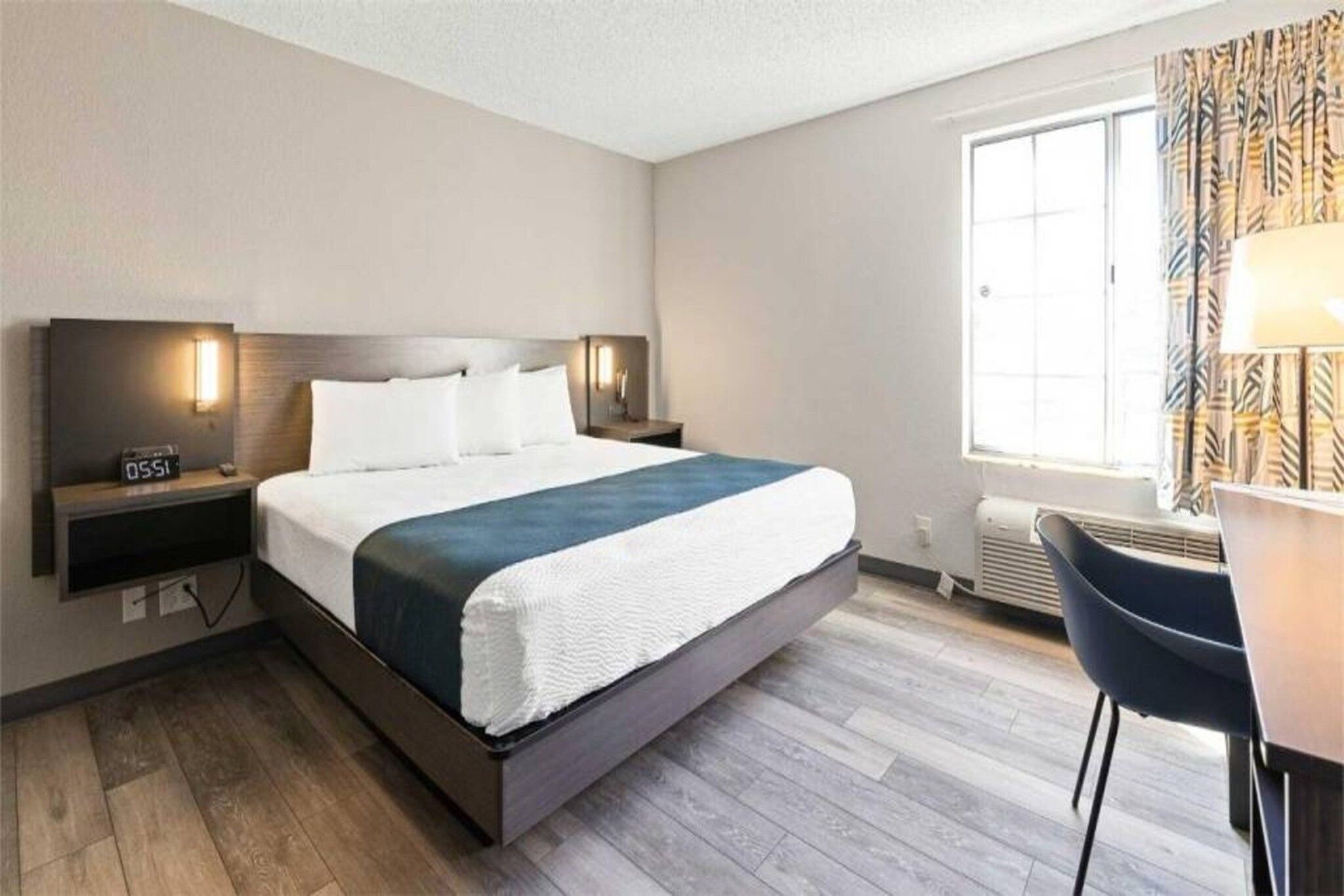 A hotel room with a bed, bedside tables, a desk, and a window.
